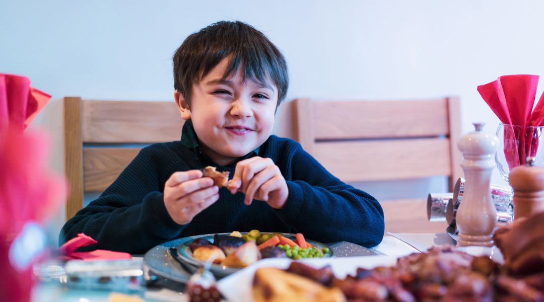 Smiling boy enjoying a meal at a dining table, surrounded by vegetables and roasted food