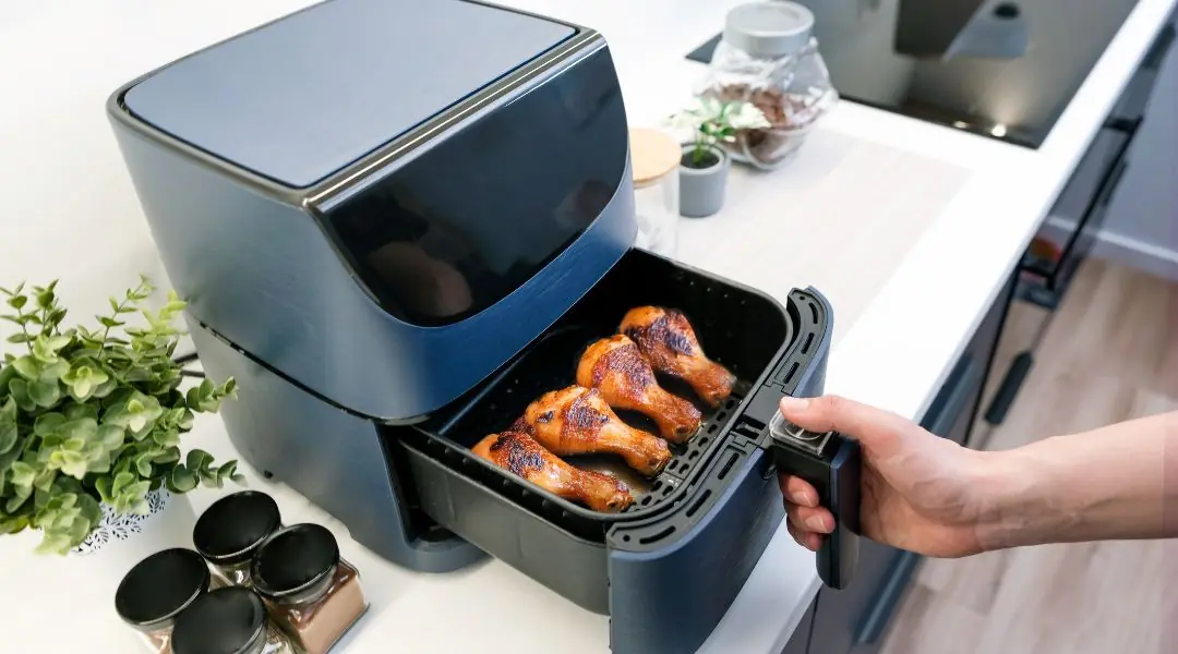 Hand taking golden chicken drumsticks out of an air fryer