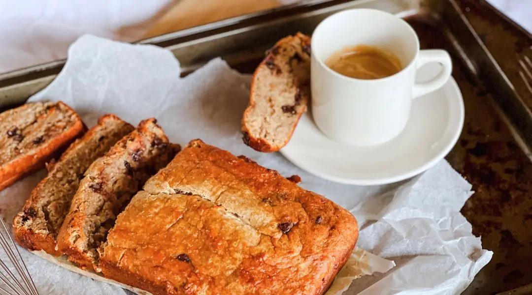 Slices of homemade banana bread with chocolate chips, served on a tray with a cup of espresso