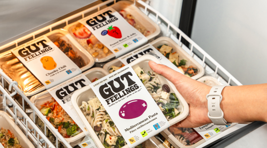 A hand holding a prepared 'Gut Feelings' meal in a freezer filled with similar meals, all labeled as FODMAP-certified.