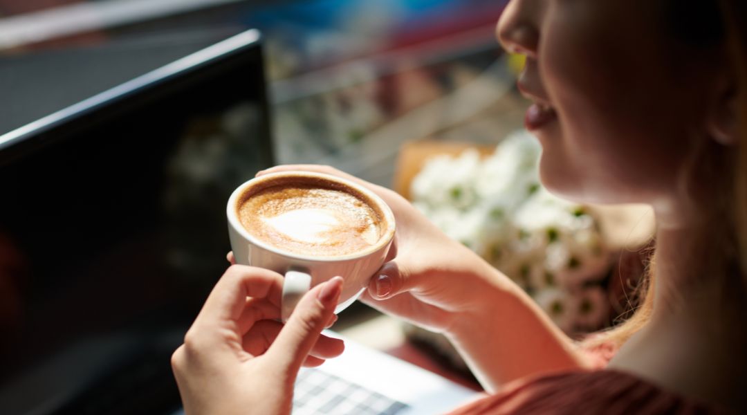 A woman holding her hot latte coffee in her hands.