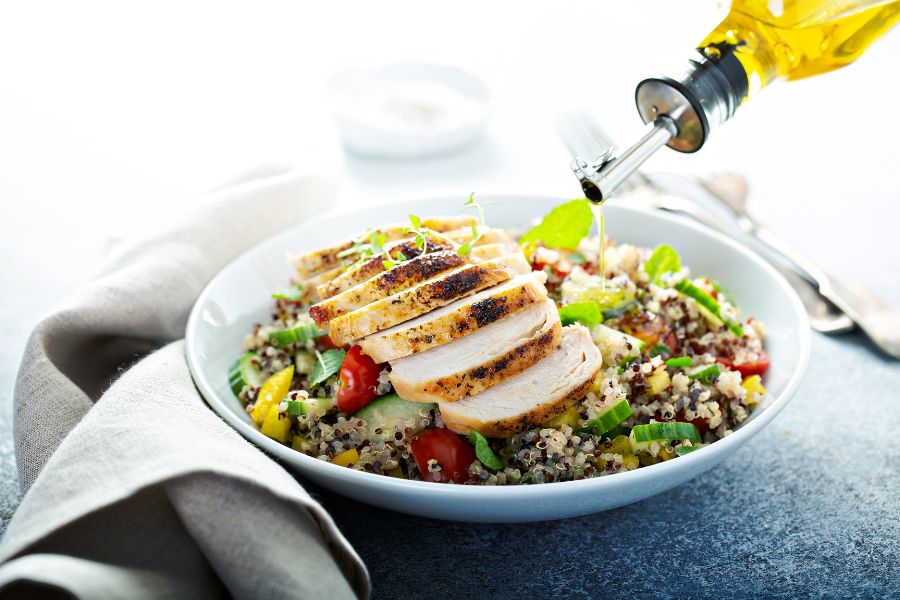 Grilled chicken slices being drizzled with olive oil over a quinoa salad