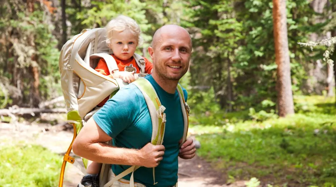 Smiling father carrying his child in a hiking backpack in the forest