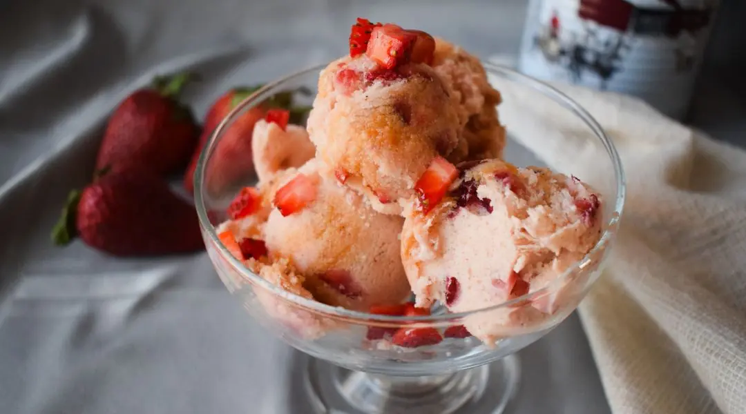 Homemade strawberry ice cream served in a cup, topped with fresh strawberries