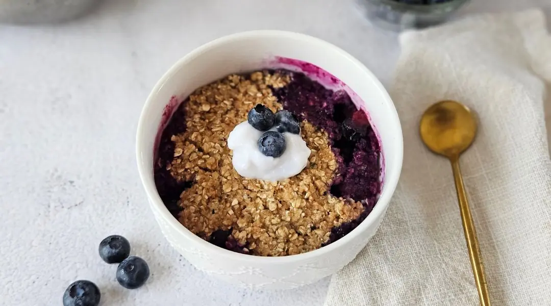 Blueberry crumble in a white bowl, topped with yogurt and fruit