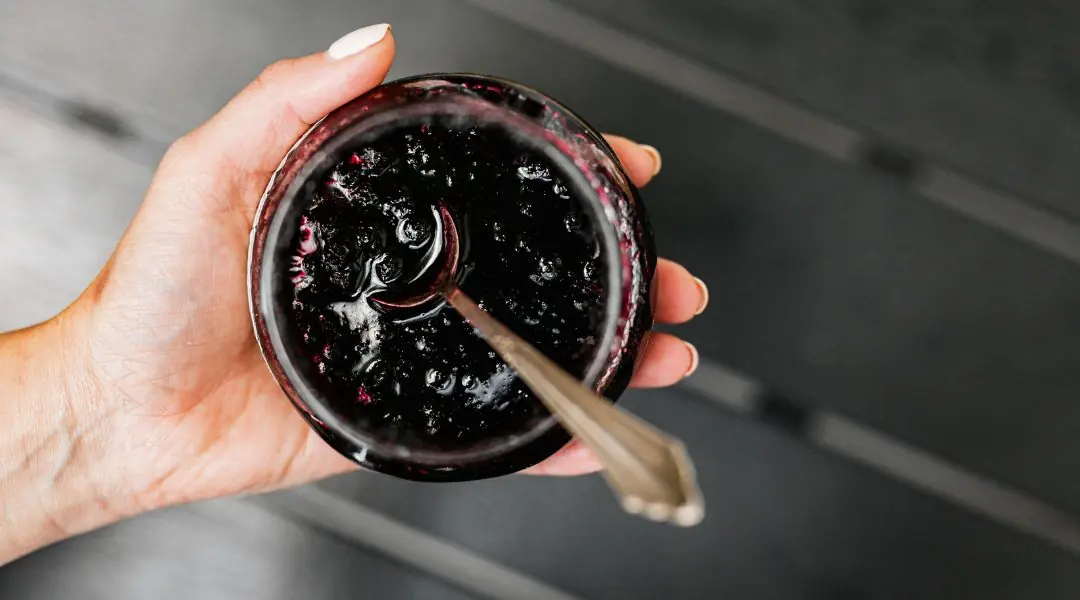 Hand holding a jar of blueberry jam with a spoon