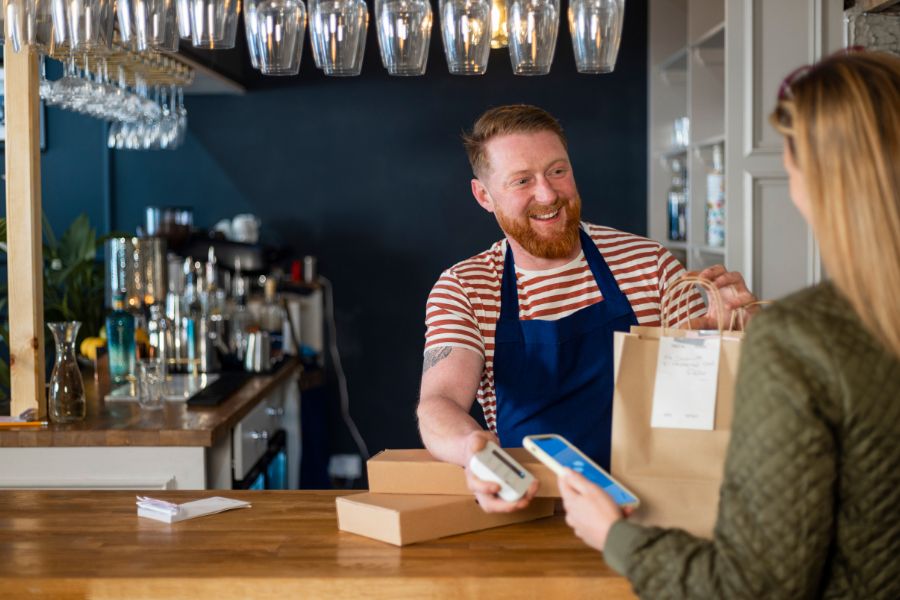 Smiling barista handing a takeout bag to a customer