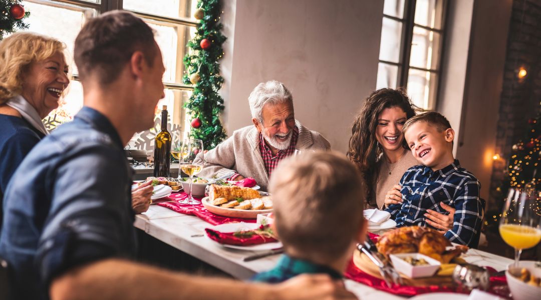 A cheerful multi-generational family enjoying a Christmas meal together, with festive decorations in the background