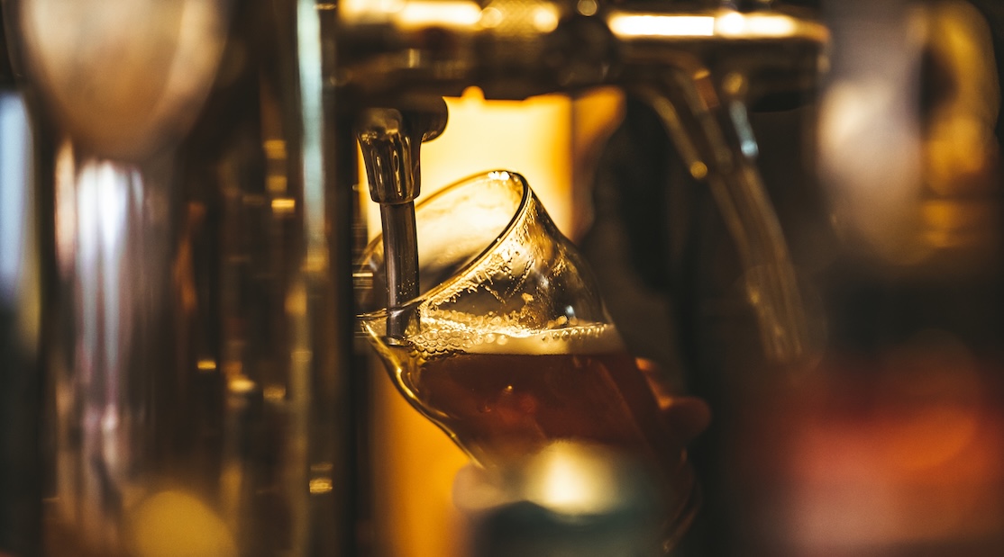 A beer glass being filled from a draft beer tap with a warm, golden light in the background.