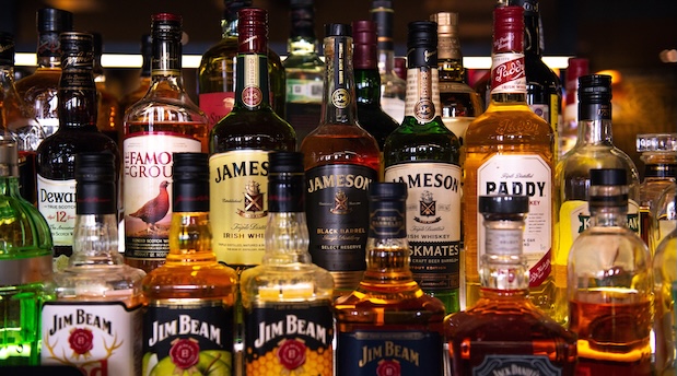 A variety of liquor bottles, including whiskey and bourbon brands, displayed on a bar shelf.