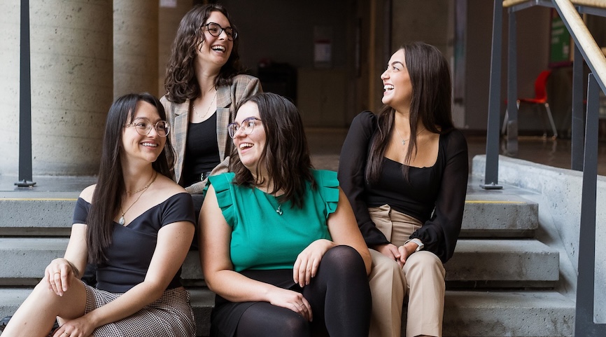 Four women dietitians sitting on stairs, smiling and laughing together in a casual and friendly atmosphere.