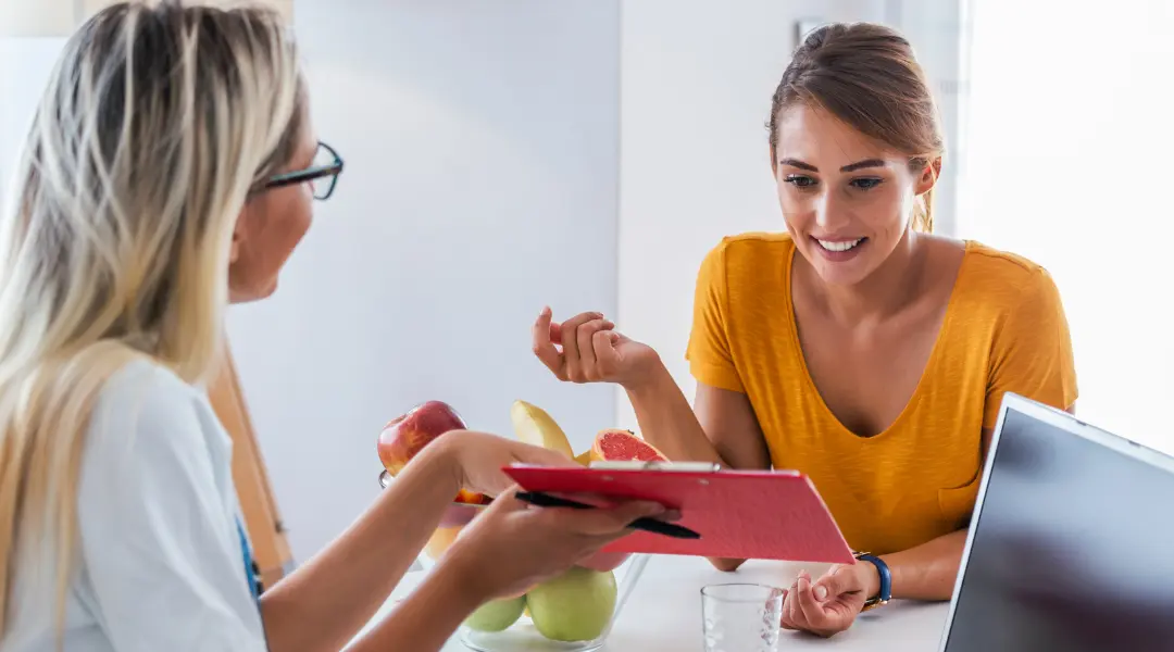 two people sitting at a table in front of a laptop