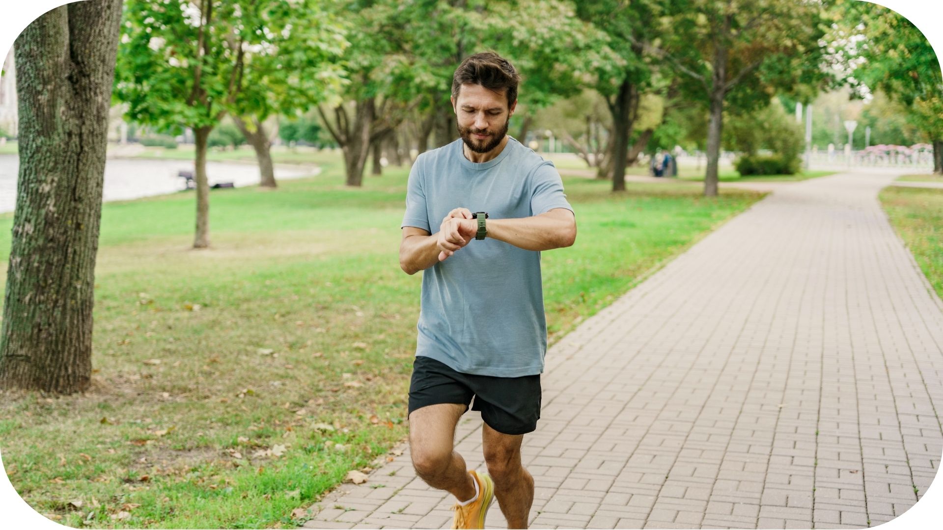 Man running in a park while checking his smartwatch, surrounded by trees and a paved path