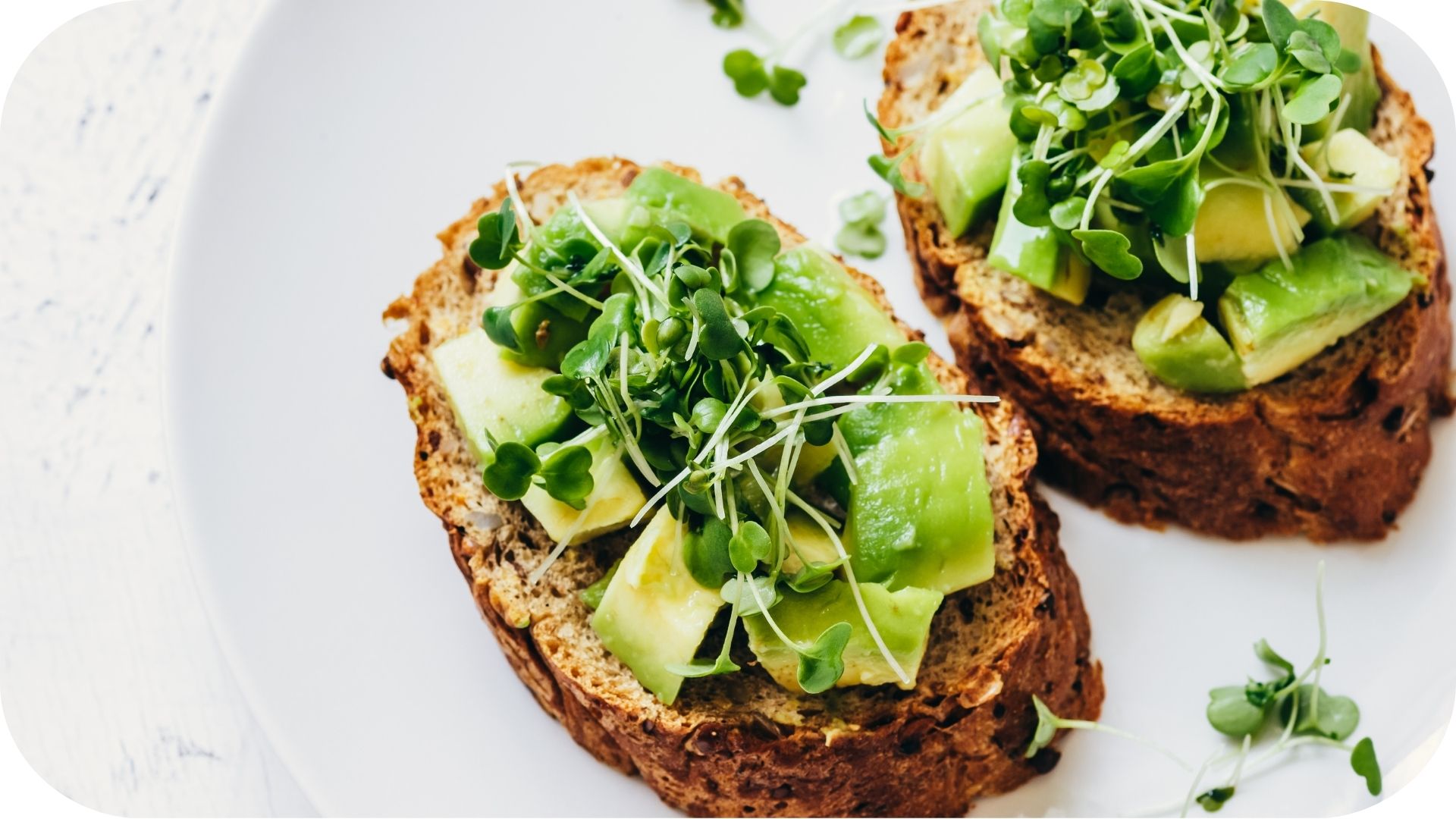 Slices of whole-grain bread topped with avocado chunks and fresh microgreens on a white plate