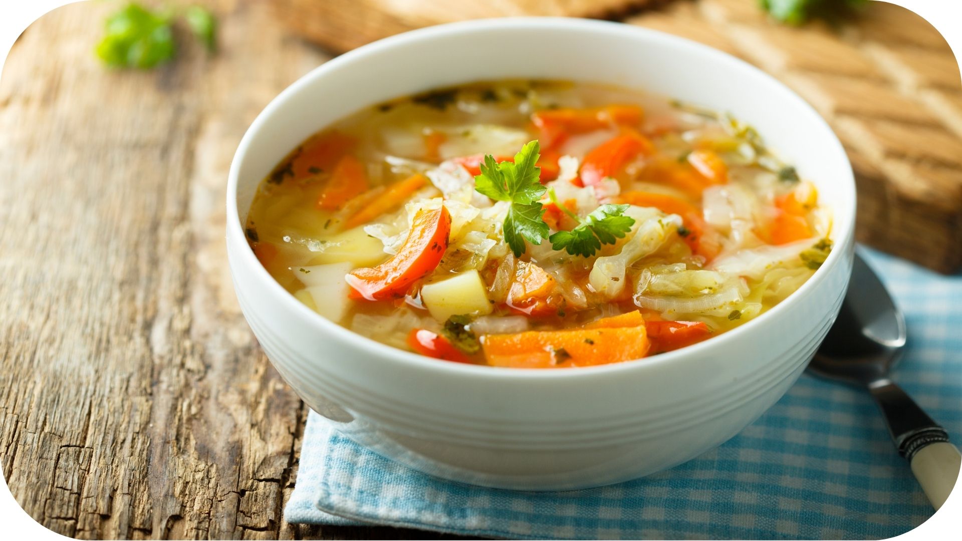 Bowl of vegetable soup with carrots, cabbage, and herbs, garnished with fresh parsley on a rustic wooden table