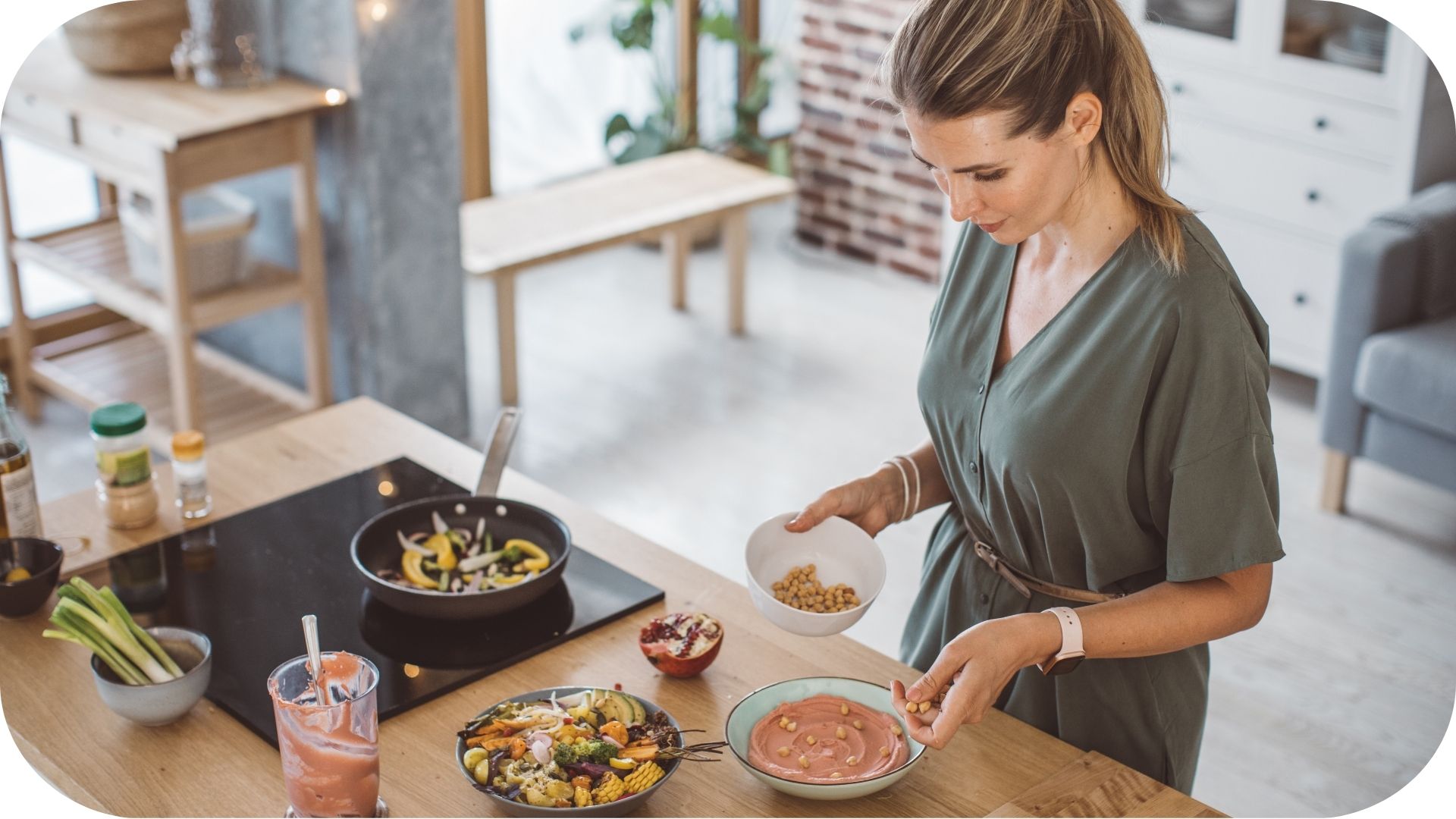 Woman preparing a meal in a modern kitchen, adding chickpeas to a bowl of hummus