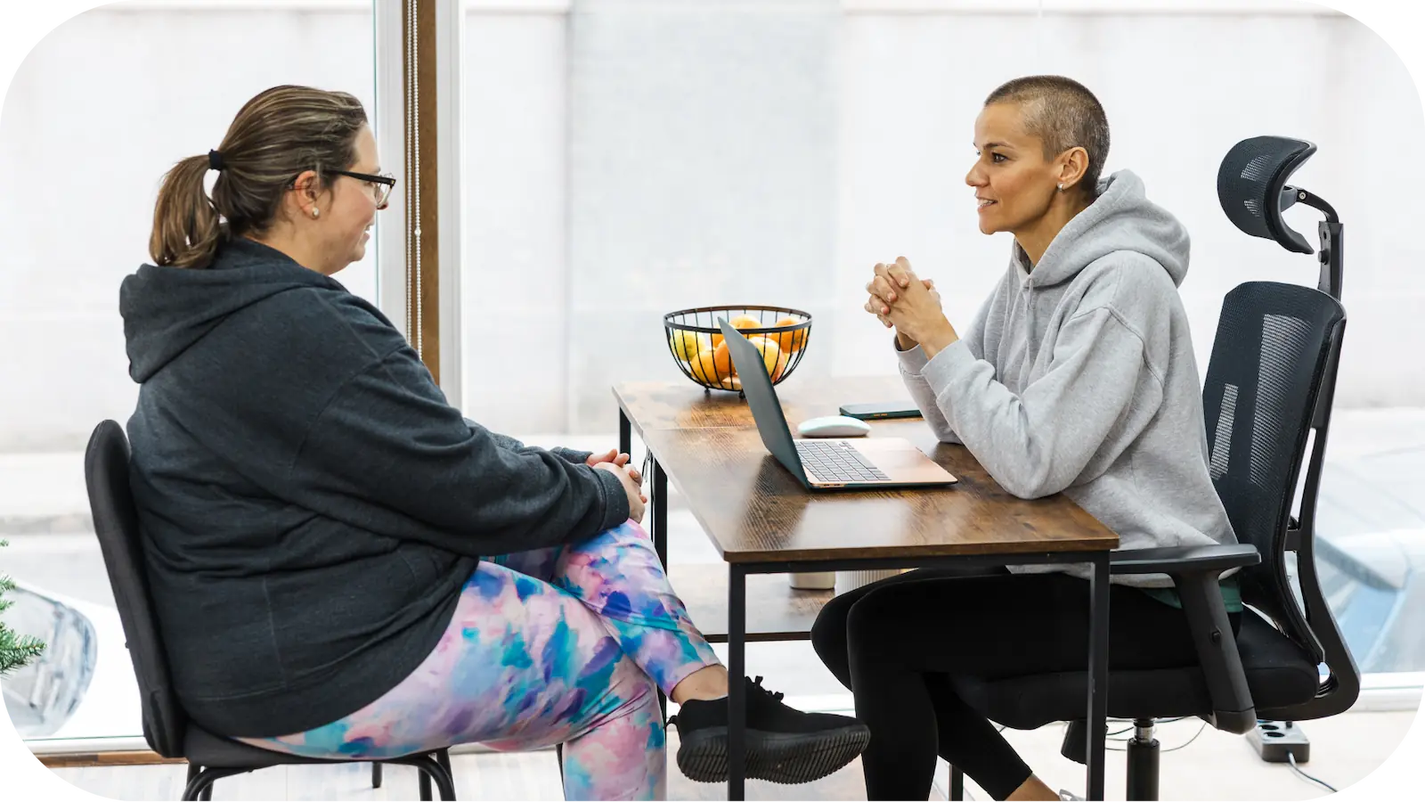 A dietitian talks with a client during a nutrition consultation, sitting across a table with a laptop and a bowl of fruit