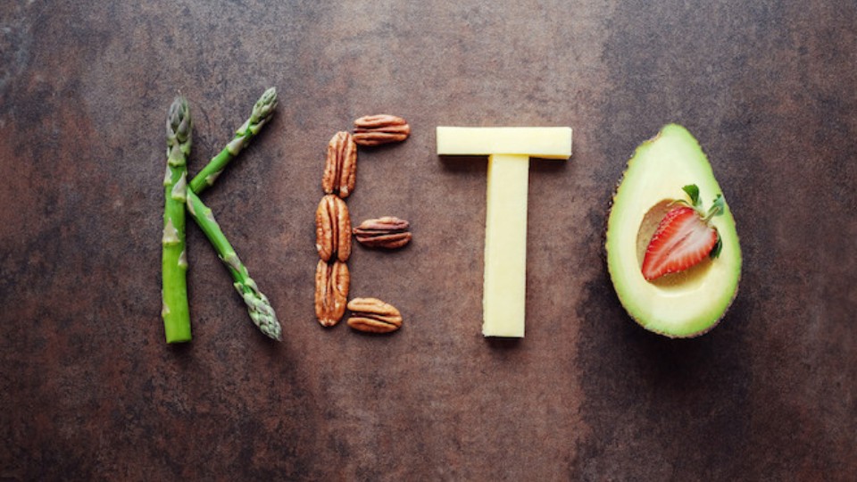 Keto written on a wooden background with vegetables and proteins