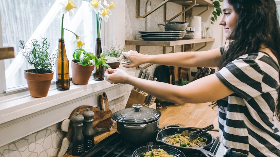 woman in a kitchen cooking a dish and adding basil