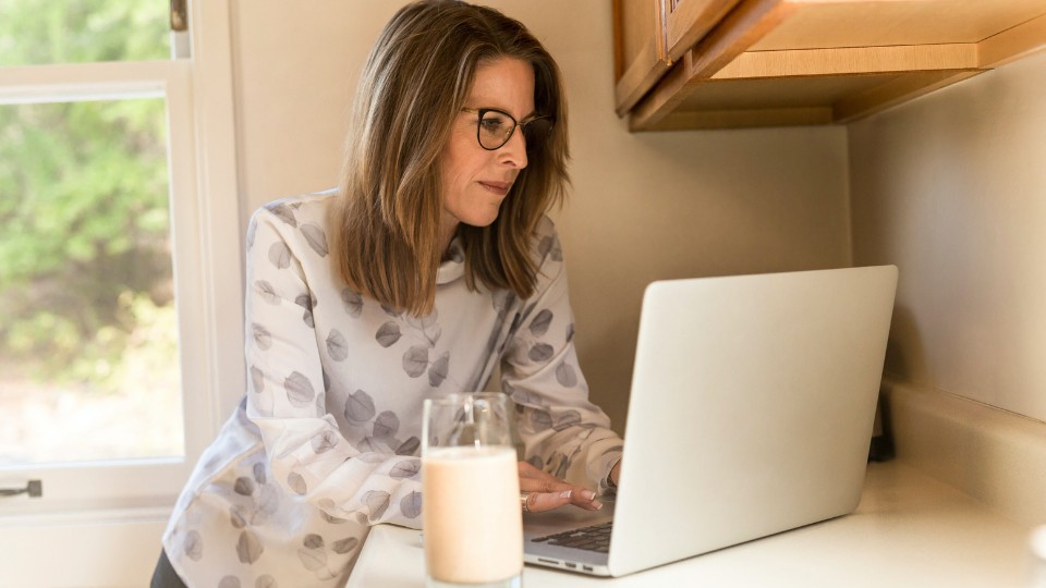 menopausal woman in front of a computer with a glass of milk