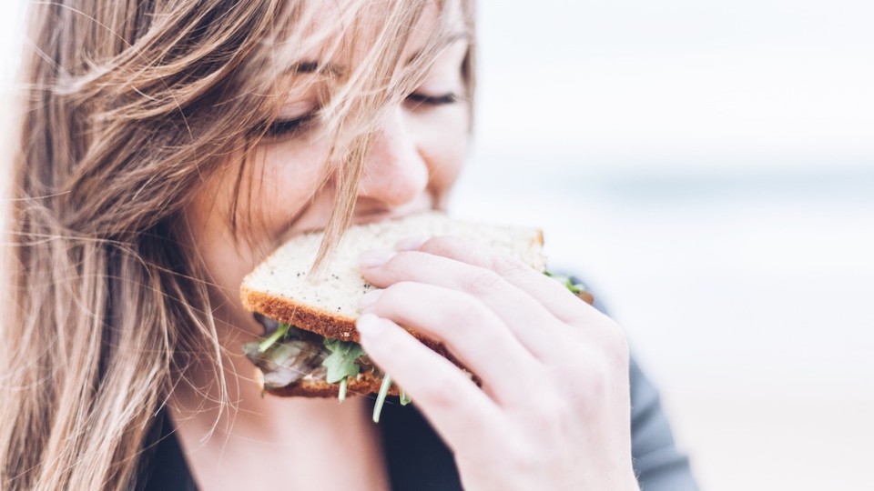 Girl eating a sandwich with wind blowing her hair