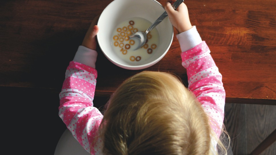 Child with a pink shirt eating cereals with milk