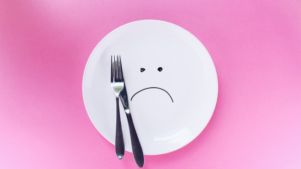 sad plate with a fork and a knife on a pink background