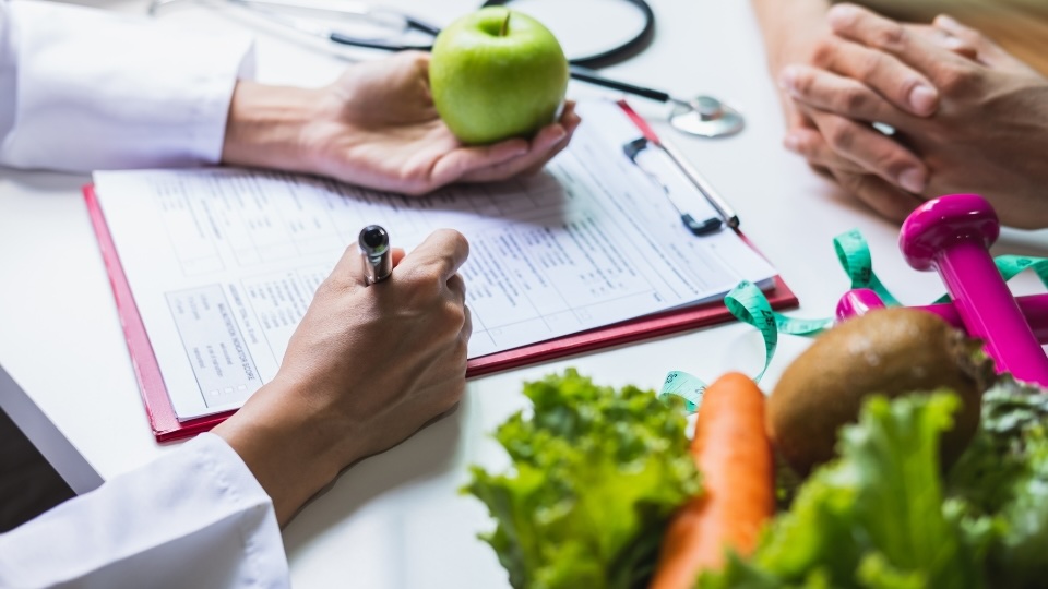 Toronto Dietitian Nutritionnist near you holding an apple and taking notes while talking to her client