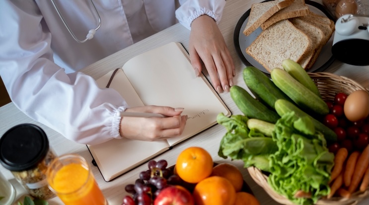 Une nutritionniste à Laval en blouse blanche écrit sur un bloc-notes entourée de fruits et légumes frais