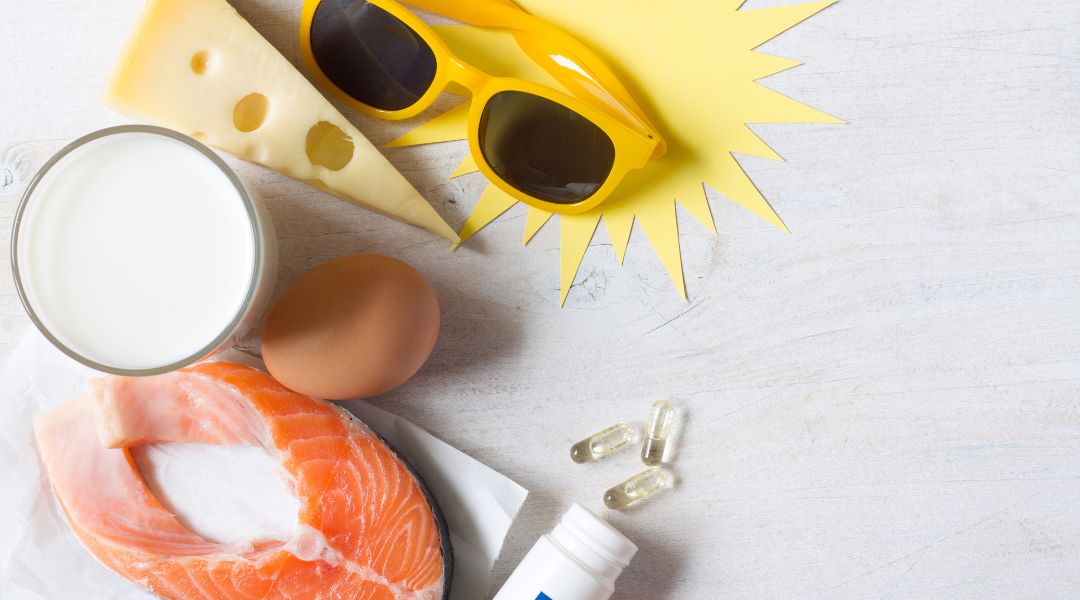 Ingredients arranged on a light surface: salmon, eggs, cheese, a glass of milk, a small bottle, and a comic-style yellow burst with sunglasses.