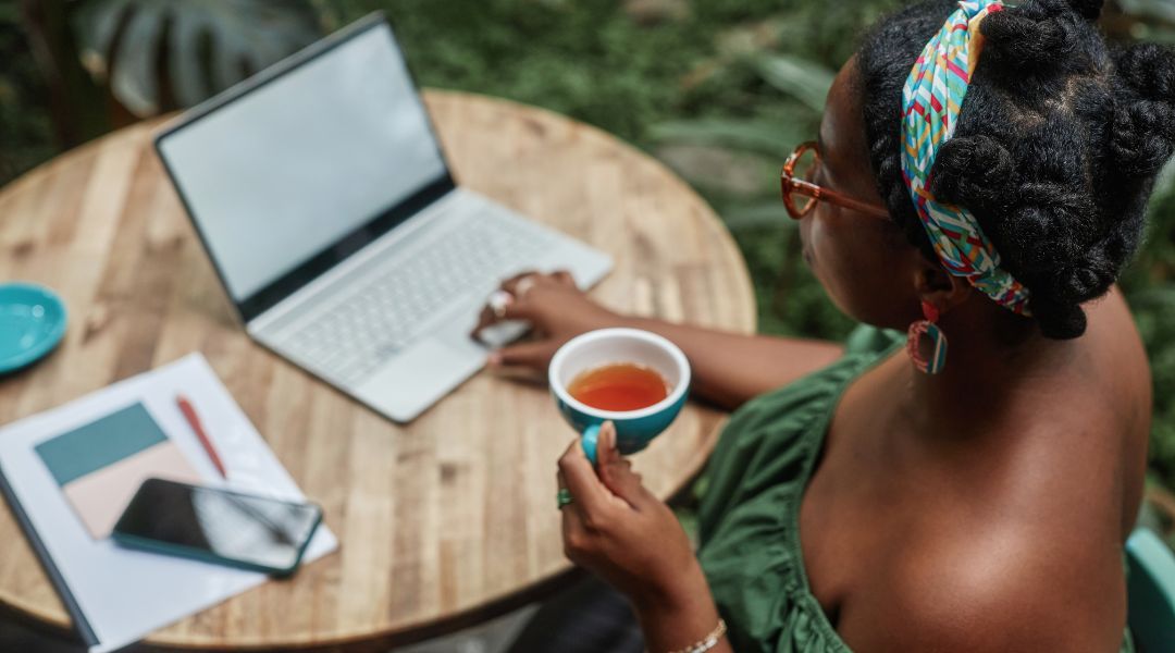 A woman drinking her hot tea while working outside in front of her computer.