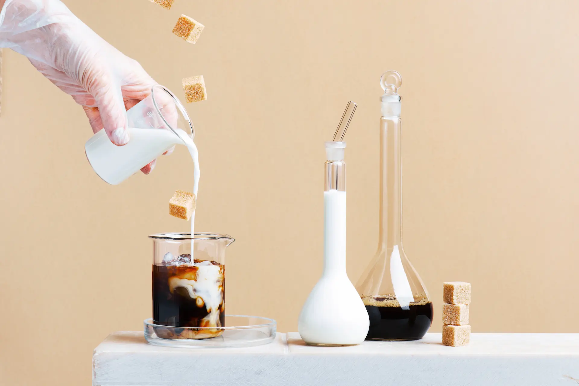 Main versant du lait dans un café glacé avec des morceaux de sucre flottants - Hand pouring milk into iced coffee with floating sugar cubes