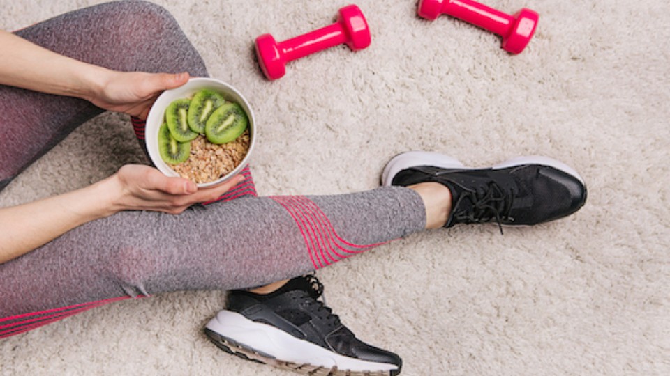 femme assise avec un bol de kiwis et deux altères rouges