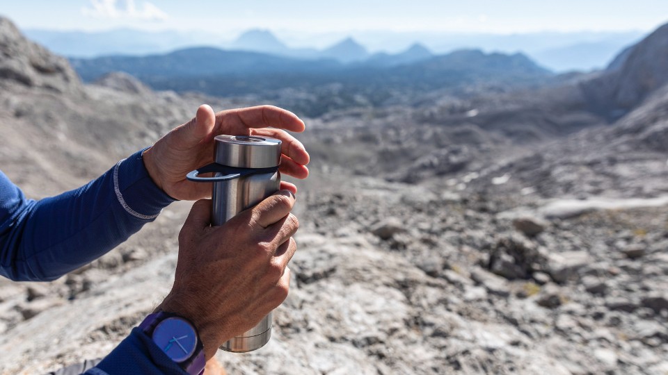 Mains ouvrant une bouteille d'eau en montagne.