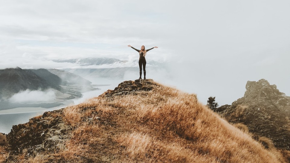 Une femme avec les bras en croix au sommet d'une montagne.