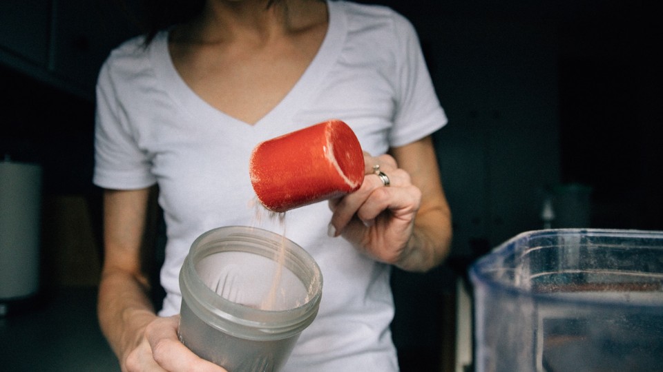 A woman putting a cup of protein powder in the blender