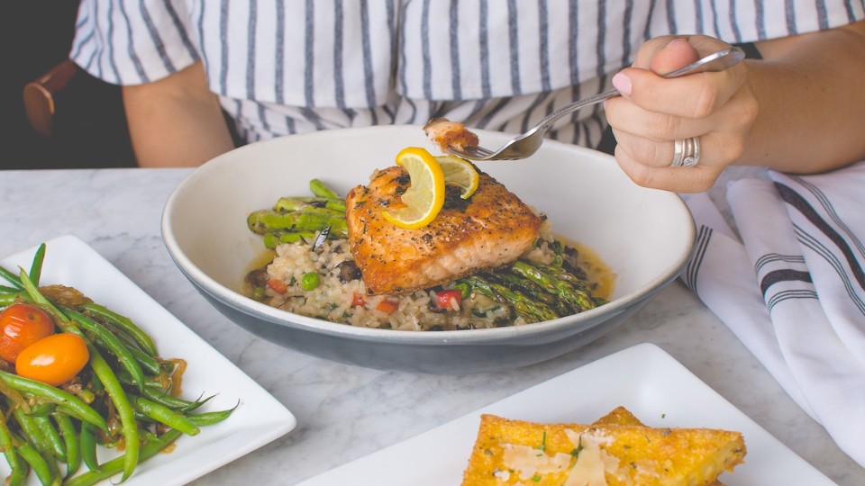 Woman eating salmon served on a bed of asparagus and rice 