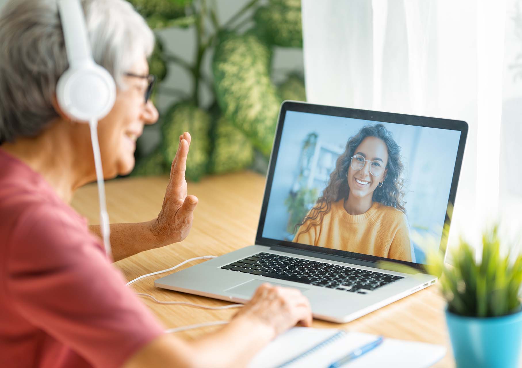 Older woman with headphones waving during a video call - Femme âgée avec des écouteurs faisant signe de la main pendant un appel vidéo