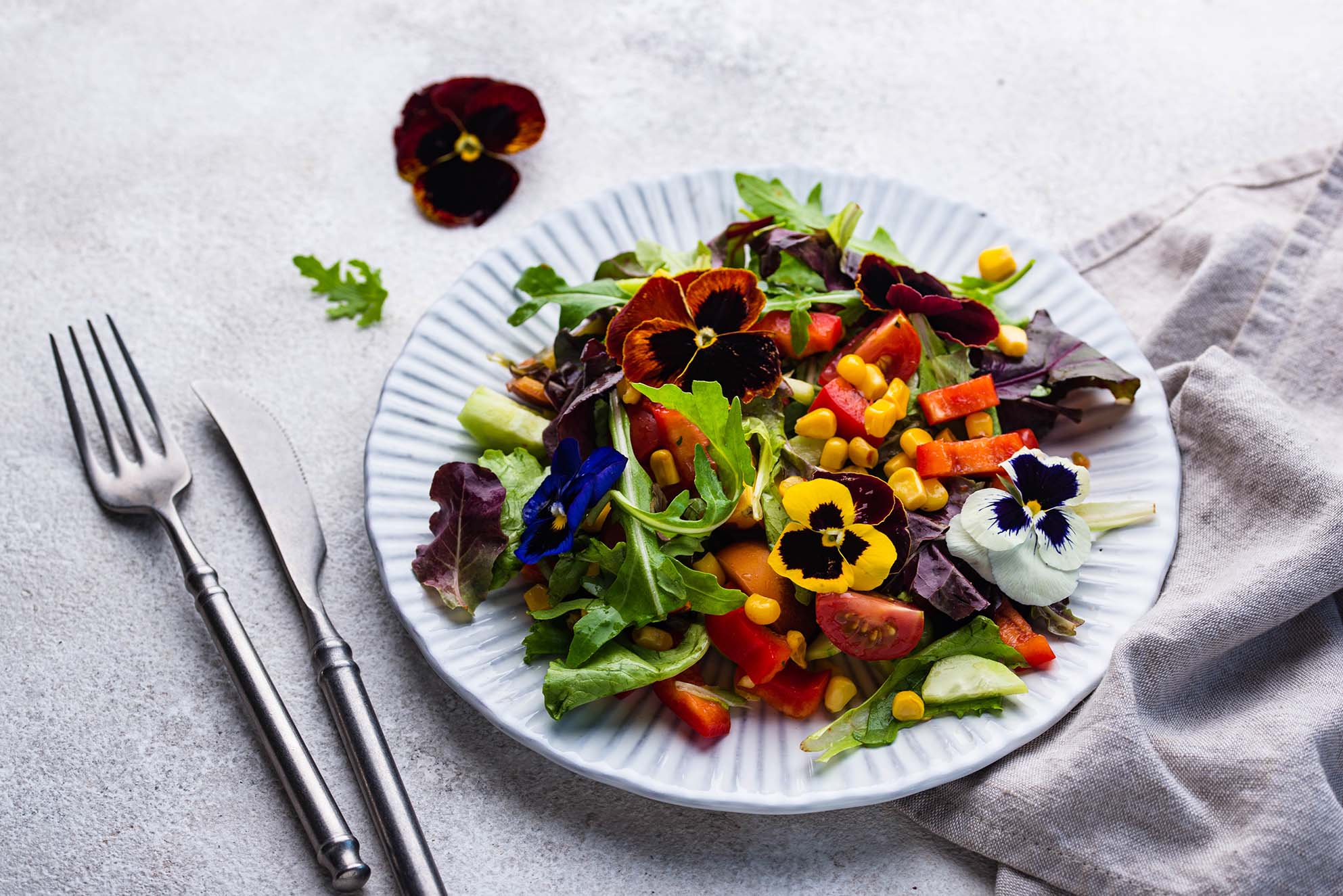 Une salade colorée garnie de fleurs comestibles, avec des légumes variés et des pensées violettes, jaunes et blanches - A colourful salad garnished with edible flowers, featuring various vegetables and purple, yellow, and white pansies