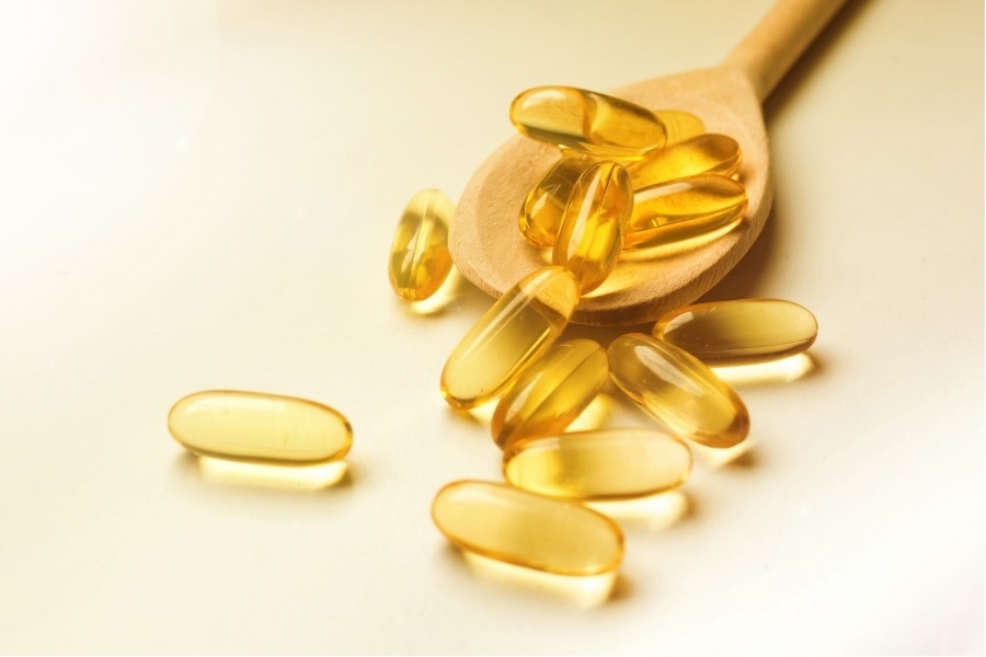 Yellow supplement capsules spilling from a wooden spoon
