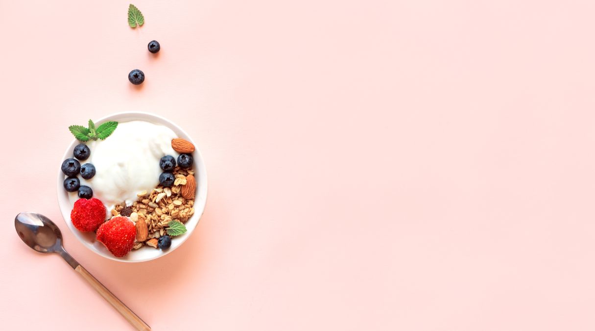 Bowl of yogurt topped with granola, blueberries, strawberries, and almonds on a pastel background