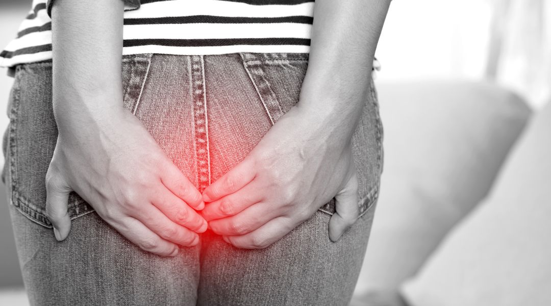 Person holding their lower back with red light highlighting discomfort in the anal area, wearing jeans