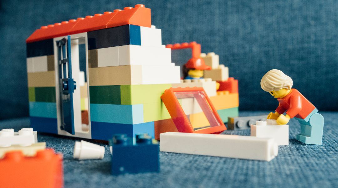 LEGO figures building a house with colorful bricks and scattered pieces on a blue surface