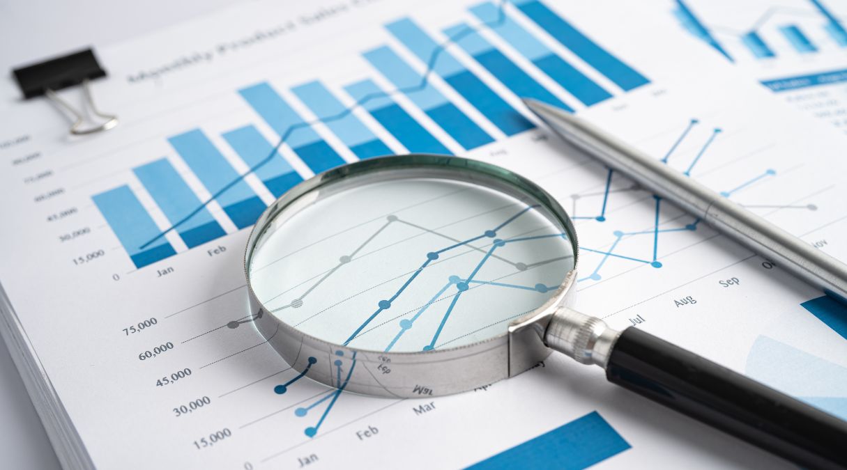 Magnifying glass over a blue and white bar graph, showing monthly sales data analysis