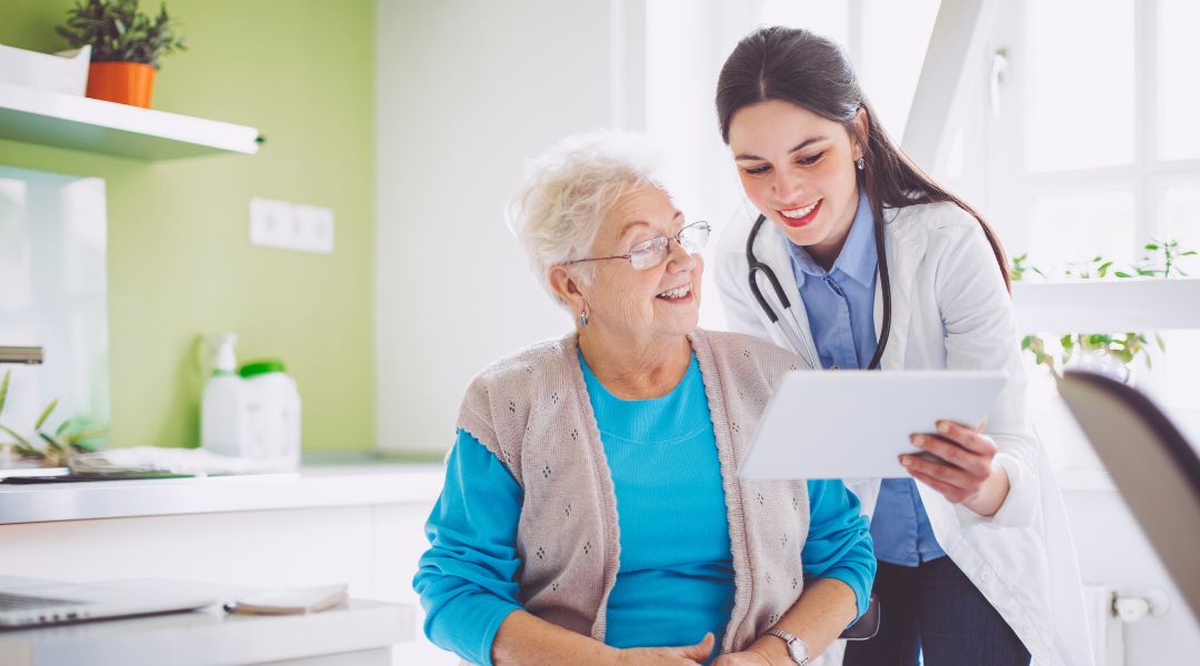 Doctor showing an elderly woman a digital tablet while they smile together in a bright, modern office