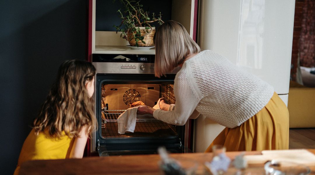 Woman and young girl baking together, placing a dish into an oven in a cozy kitchen