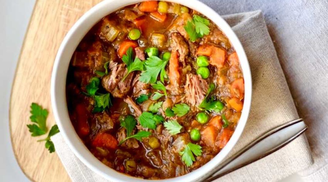 A bowl of beef stew with carrots, peas, and fresh parsley on a wooden surface - TeamNutrition Recipe