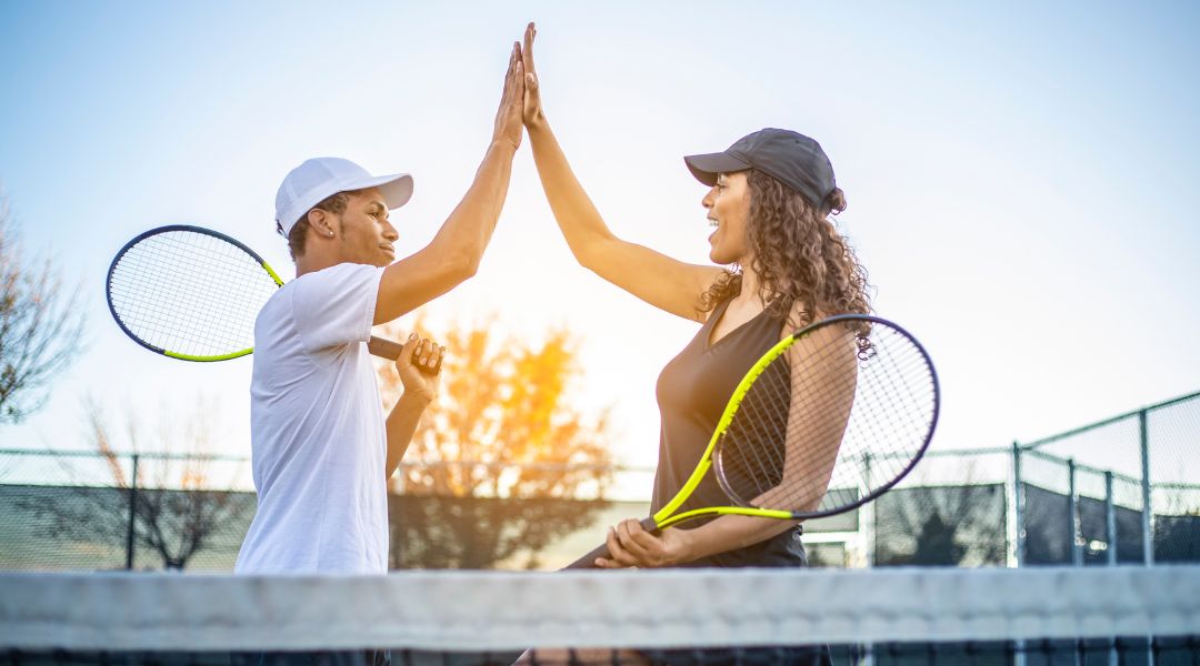 A pair giving each other a high five on a tennis court.