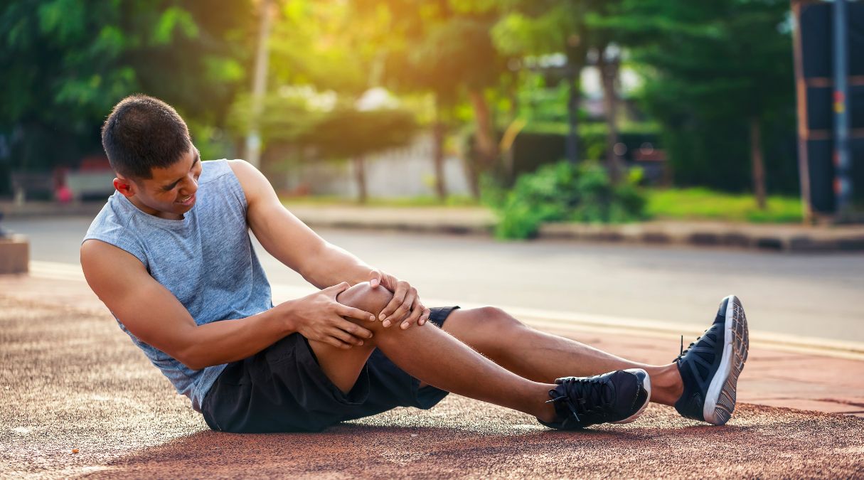 Man sitting on the ground holding his knee in pain, indicating a possible sports injury