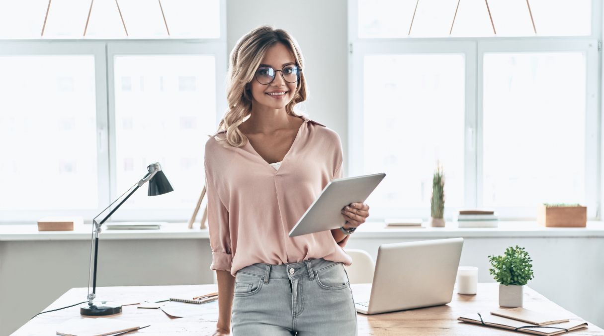 Smiling dietitian in a light pink blouse holding a tablet in a bright, modern office